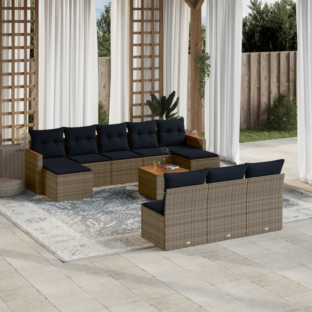Garten-Sitzgruppe mit schwarzen Kissen, Couchtisch und Teppich auf einer Terrasse. Weiße Vorhänge und Holzgitter im Hintergrund.