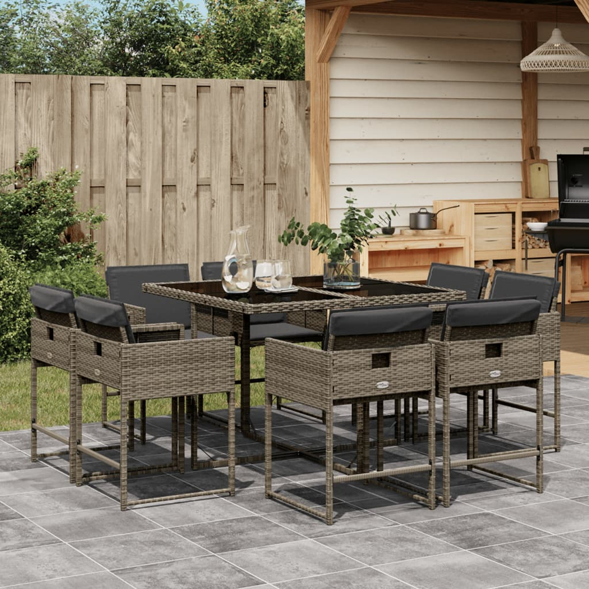 Essgruppe im Freien auf einer Terrasse. Sie verfügt über einen Tisch, Stühle und eine Wasserkaraffe. Holzzaun und -struktur im Hintergrund.