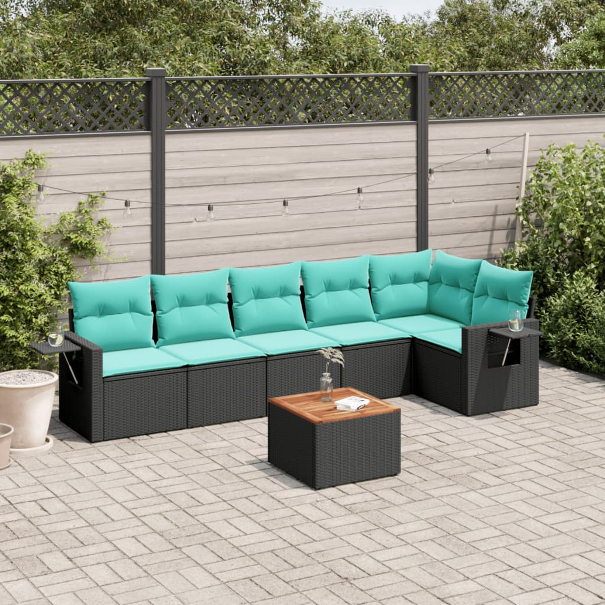 Gartensofa mit türkisfarbenen Kissen und einem Holztisch auf einer Backstein-Terrasse. Im Hintergrund sind Zaun und Grün zu sehen.