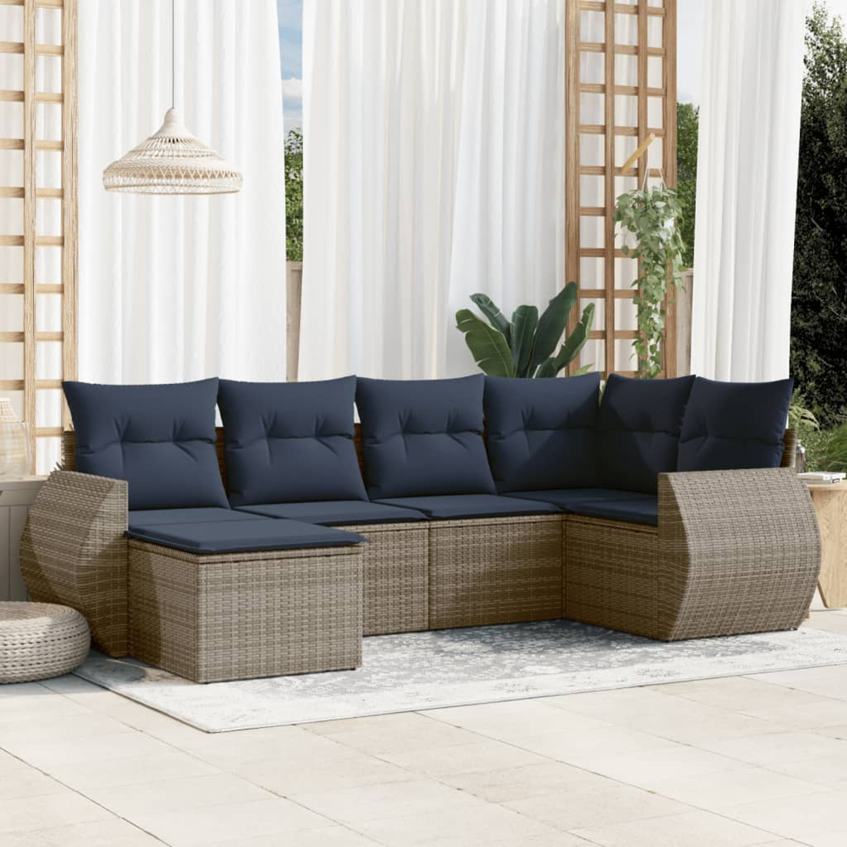 Sofá seccional exterior con cojines azul marino en un patio. Cortinas blancas y una lámpara colgante. El fondo incluye un enrejado y plantas.