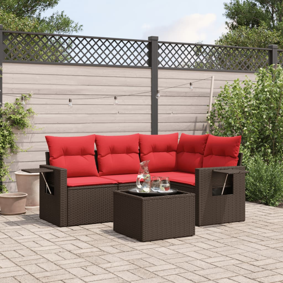 Garten-Sofa mit roten Kissen. Vor dem Sofa steht ein Glastisch mit Getränken. Im Hintergrund ein Zaun und Pflanzen.