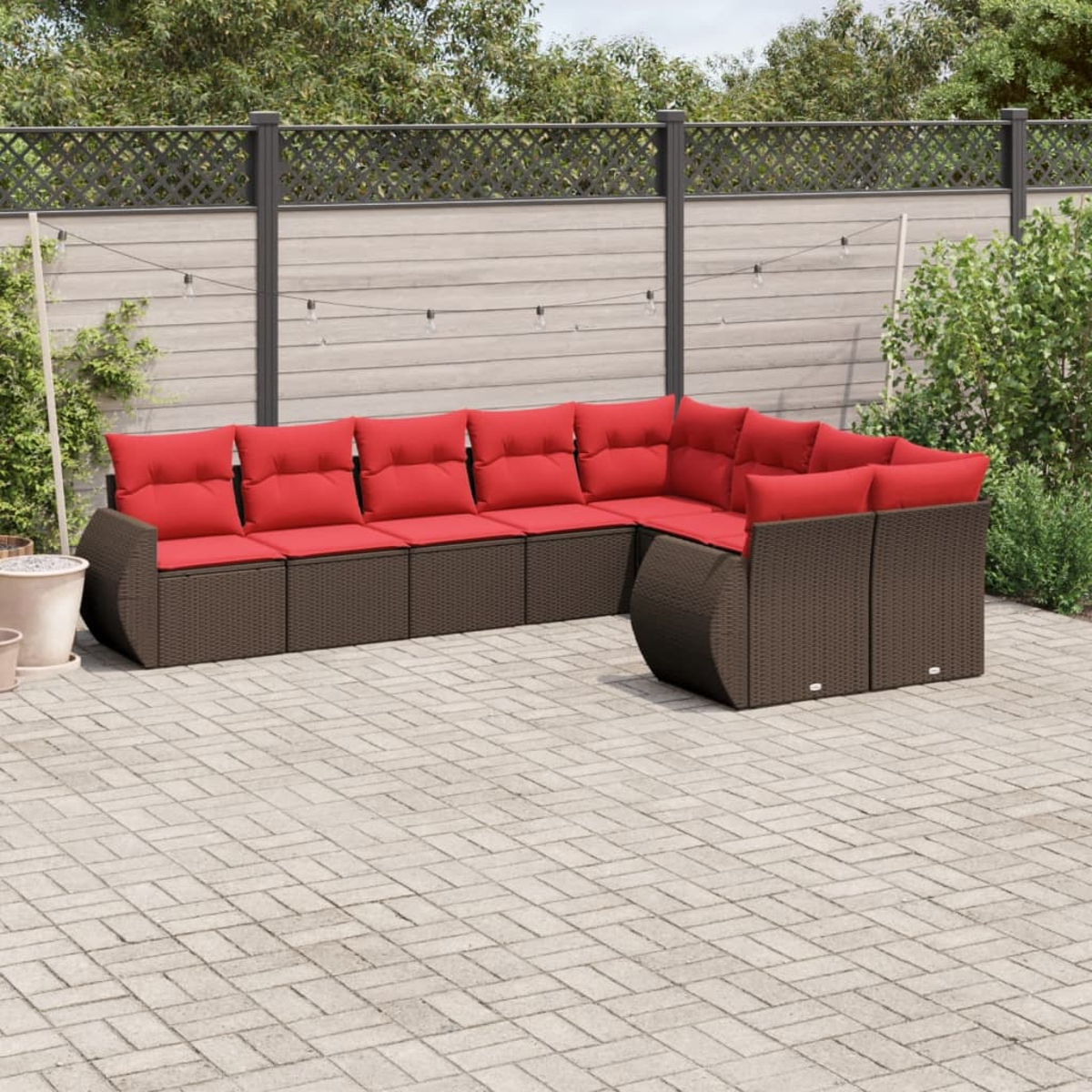 Ein Ecksofa mit roten Kissen im Freien steht auf einer Terrasse. Dahinter sind ein Zaun und Grün. Die Terrasse ist gemauert.