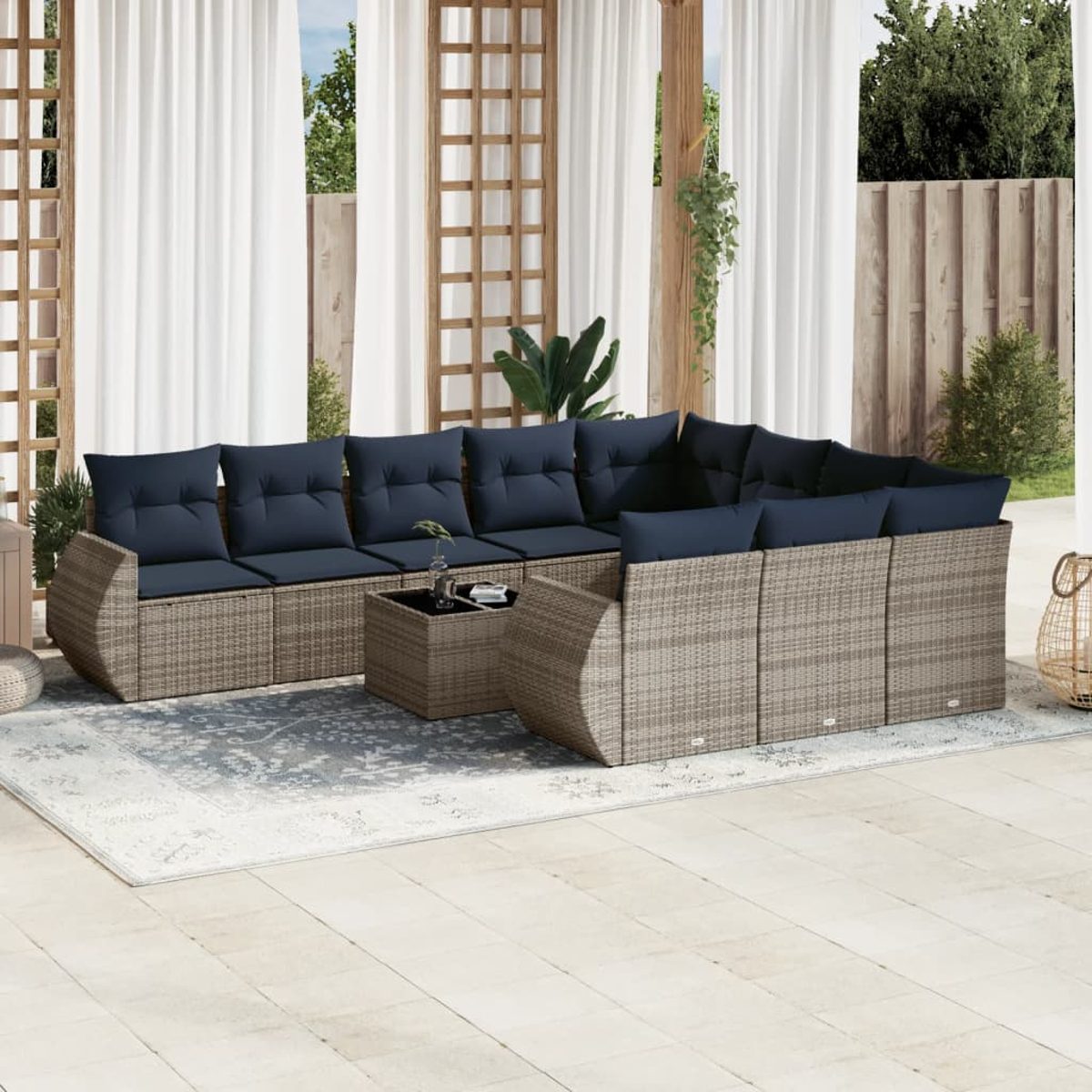 Gartenmöbel mit blauen Kissen. Davor steht ein Couchtisch. Weiße Vorhänge, Holzstruktur und Grün im Hintergrund.