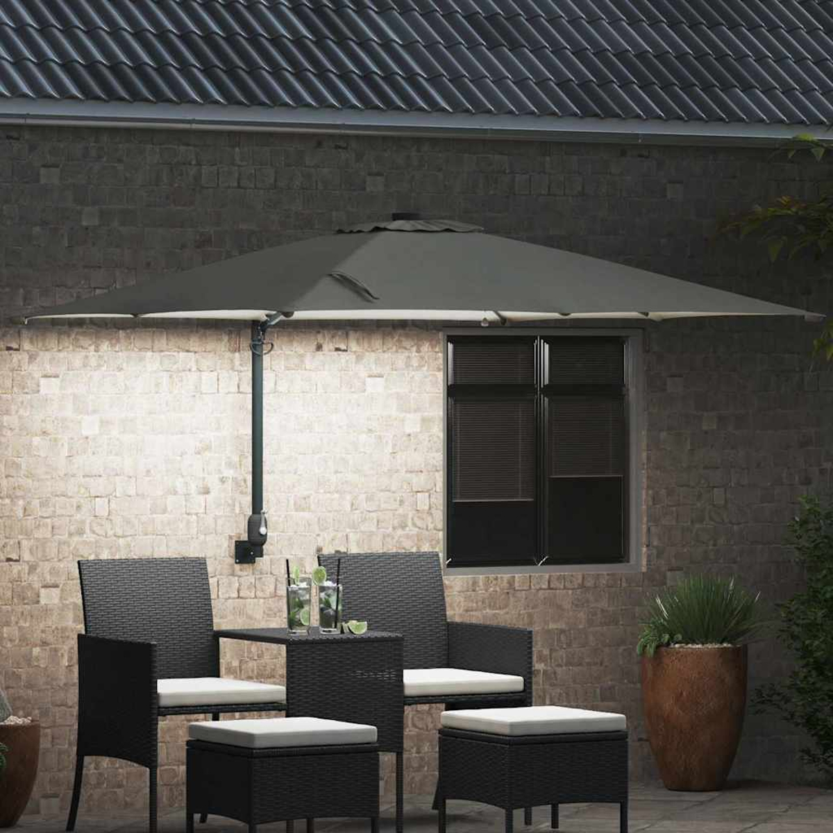 Scena all'aperto con mobili da patio neri, un ombrellone grigio e un muro di mattoni con una finestra. Bevande con lime sul tavolo.
