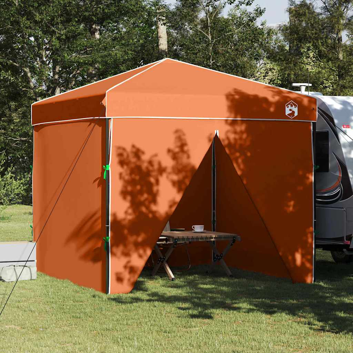 Ein orangefarbenes Zelt steht auf Gras. Ein Tisch mit einer Tasse steht darin. Ein Camper steht hinter dem Zelt. Bäume sind im Hintergrund.