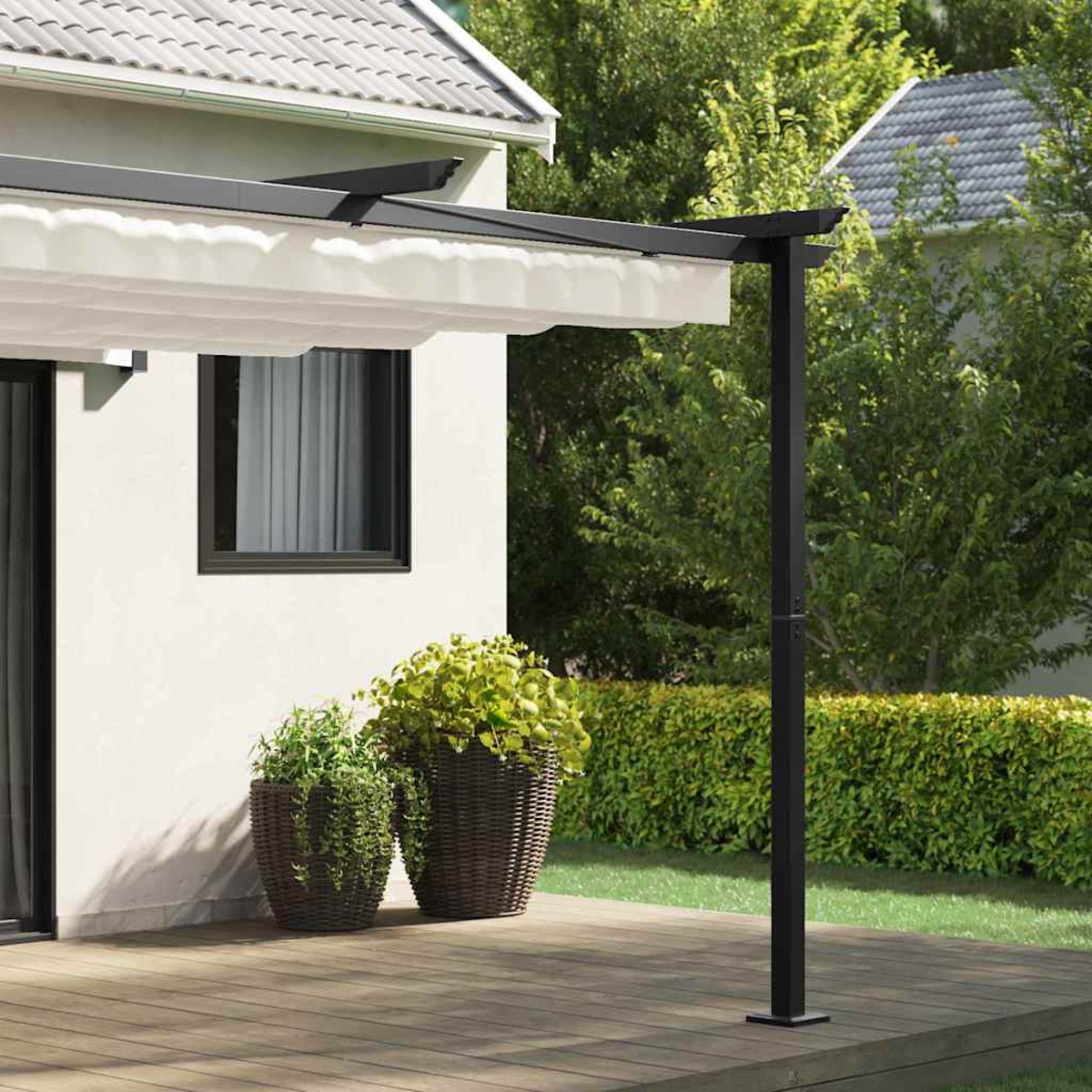Ein weißes Haus mit schwarzer Pergola, zwei Topfpflanzen und einer Holzterrasse. Grüne Büsche und Bäume im Hintergrund.