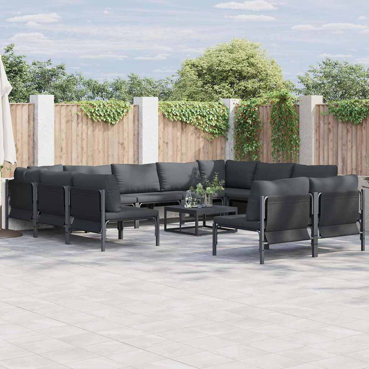 Gartenmöbel-Set mit Ecksofa, Stühlen und Couchtisch. Holzzaun und Grün im Hintergrund.