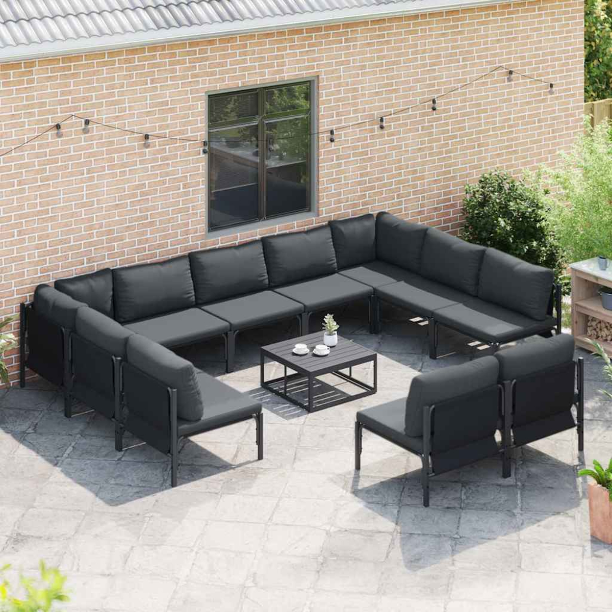 Terrassenszene mit dunkelgrauem Ecksofa, quadratischem Couchtisch und zwei Stühlen. Hintergrund Backsteinmauer.