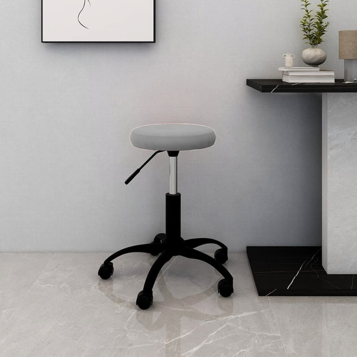 Un taburete gris con patas negras está frente a una pared. Al fondo, hay una mesa y un cuadro enmarcado.