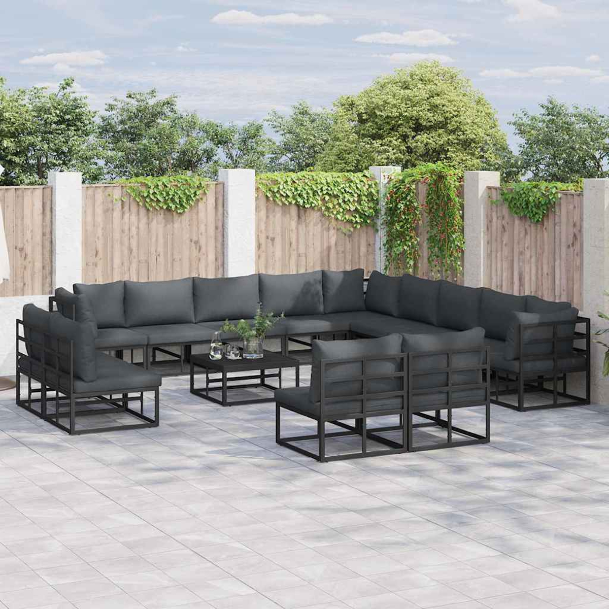 Outdoor-Terrassenset mit dunkelgrauen Kissen. Enthält Sofas, Stühle und einen Couchtisch auf einer gefliesten Terrasse. Grünes Laub dahinter.