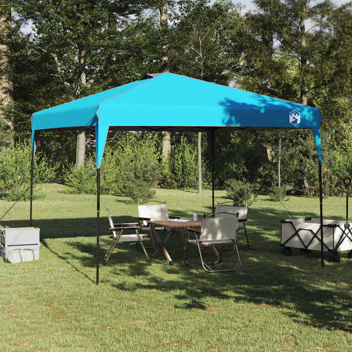Una tenda turchese ripara un tavolo e delle sedie sull'erba. Due carrelli sono ai lati. Gli alberi riempiono lo sfondo.