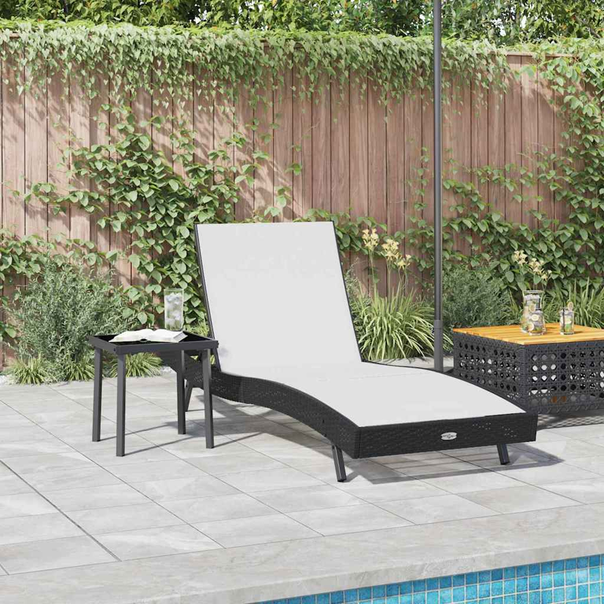 Eine schwarze Korbliege mit weißem Kissen steht am Pool. Daneben steht ein kleiner Tisch mit einem Buch und einem Glas, in einem Garten.