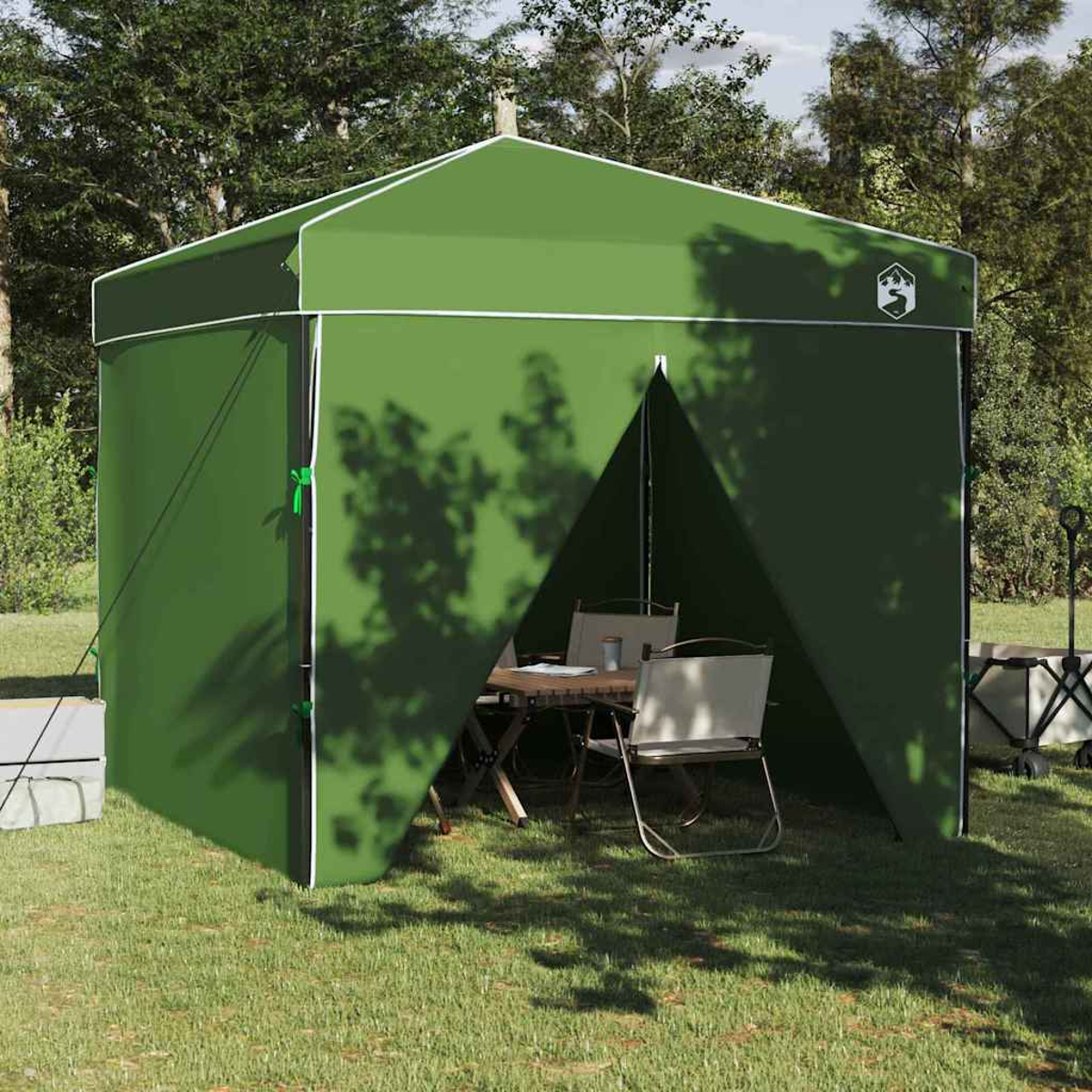 Un rifugio verde per campeggio con finiture bianche si trova sull'erba. All'interno ci sono un tavolo e sedie. Gli alberi sono sullo sfondo.