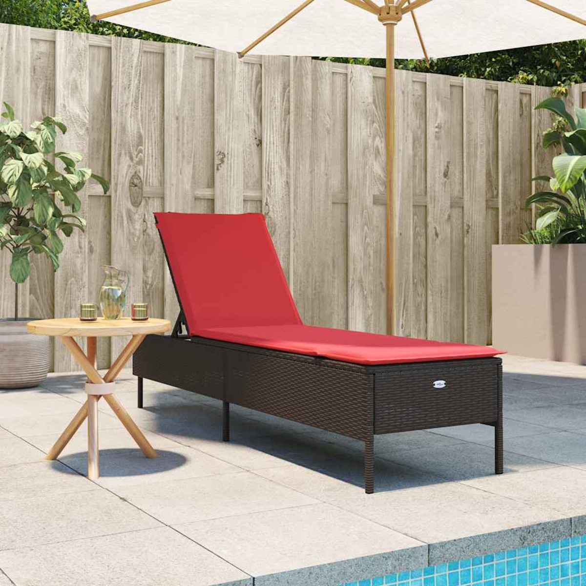 Eine Liege mit rotem Kissen steht am Pool. Ein kleiner Tisch mit Krug und Gläsern befindet sich in der Nähe. Ein Sonnenschirm spendet Schatten.