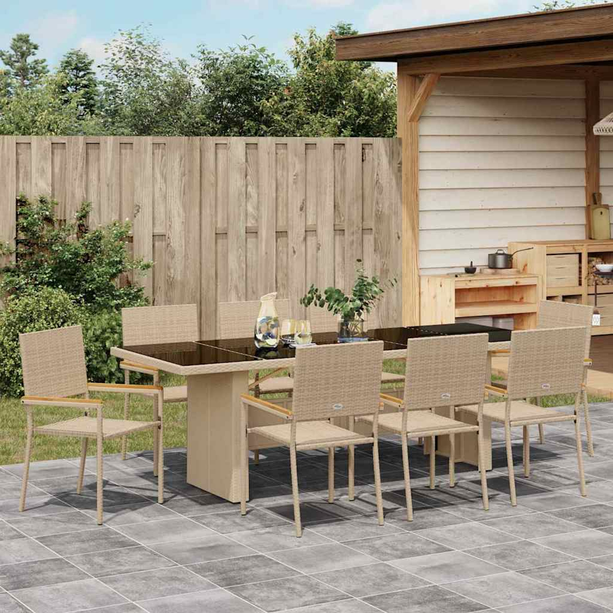 Juego de comedor al aire libre con mesa de cristal y sillas beige. Una valla de madera y una pequeña cocina al fondo.