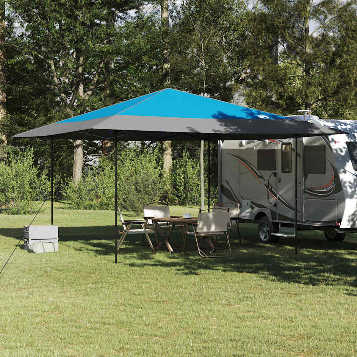 Una scena di campeggio con una tenda da sole blu e grigia, tavolo, sedie e camper. Alberi sullo sfondo su un prato.