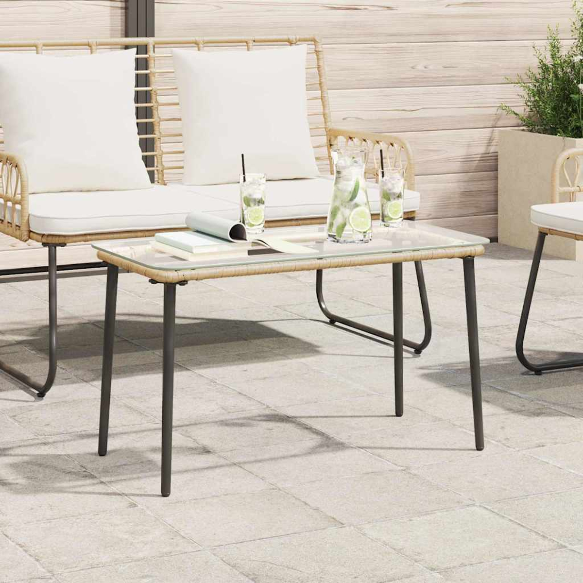 Escena al aire libre con muebles de mimbre, mesa de vidrio con bebidas y cojines blancos. Fondo con pared de madera y planta en maceta.