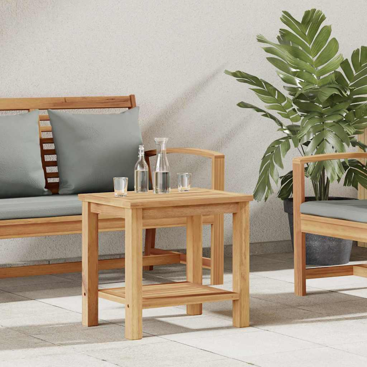 Mesa de madera con botellas de agua y vasos. Un banco y una silla con cojines grises detrás. Una planta grande a la derecha.