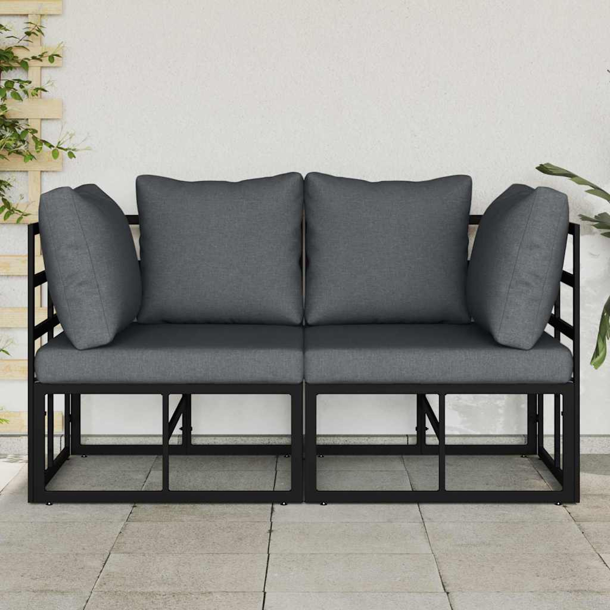 Zweisitziges Outdoor-Sofa mit grauen Kissen auf einem schwarzen Metallrahmen. Vor einer weißen Wand und gefliesten Terrasse.