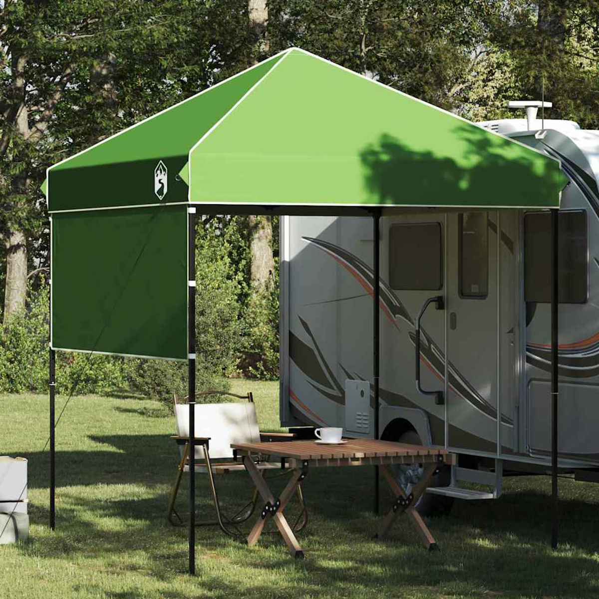 Ein grünes Vordach mit Tisch, Stühlen und einem Wohnmobil im Hintergrund, auf einer Wiese im Freien.