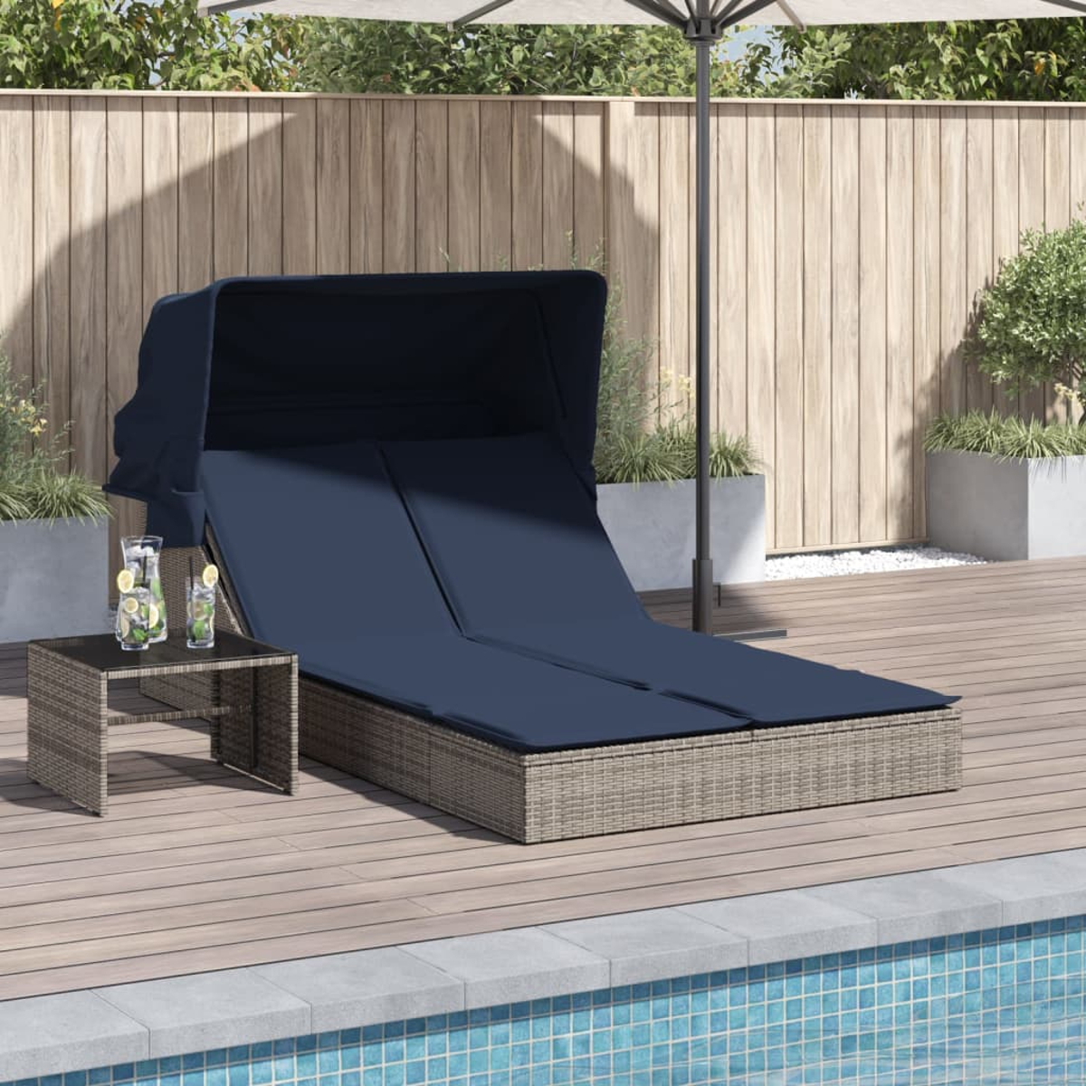 Ein dunkelblau gepolstertes Tagesbett im Freien unter einem Baldachin mit einem kleinen Tisch mit Getränken. Es befindet sich auf einem Holzdeck neben einem Pool.