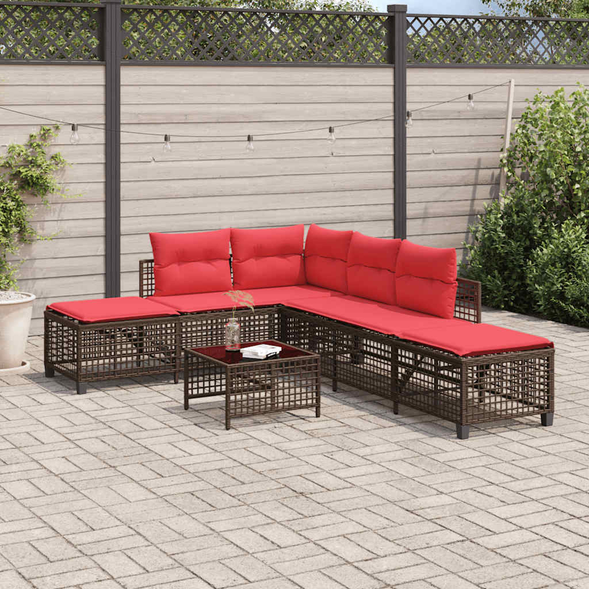 Outdoor-Ecksofa mit roten Kissen und einem kleinen Tisch auf einer gepflasterten Terrasse. Im Hintergrund ein Holzzaun und Pflanzen.