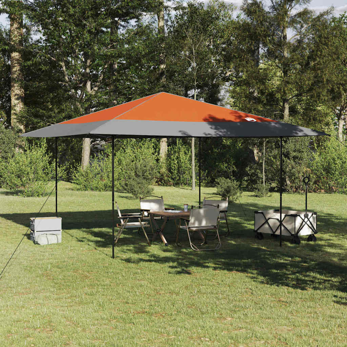 Una scena all'aperto con un gazebo, un tavolo, sedie e un carrello sull'erba. Gli alberi sono sullo sfondo. Il gazebo ha colori arancione e grigio.