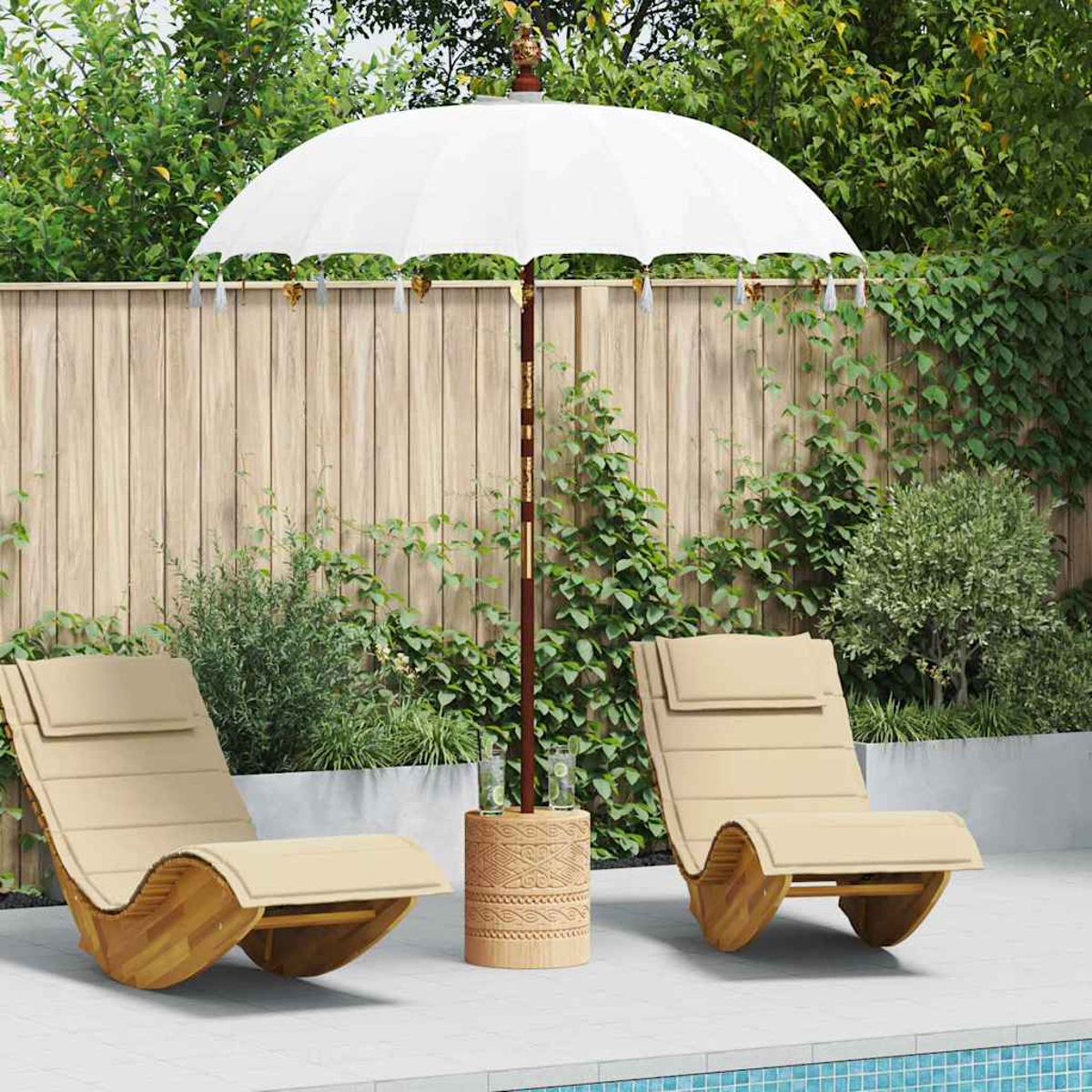 Scena all'aperto con due sedie a sdraio beige, un ombrellone bianco e un tavolino di legno vicino a una piscina. Piante verdi e staccionata di legno sullo sfondo.
