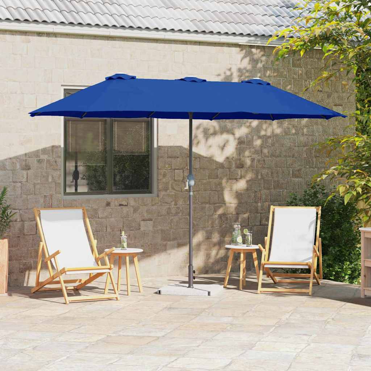 Un ombrello blu ombreggia due sedie e tavolini. Un muro di pietra e vegetazione sullo sfondo creano un'atmosfera da patio.