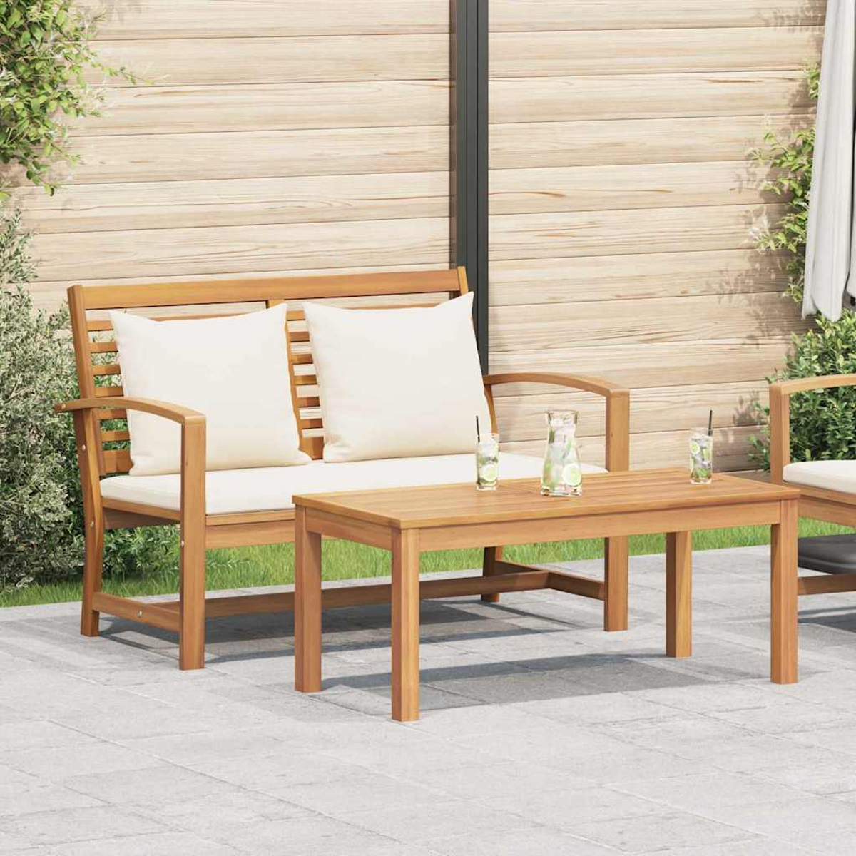 Gartenmöbel-Set aus Holz mit weißen Kissen und einem kleinen Tisch, Getränke stehen auf dem Tisch, im Hintergrund eine Holzwand.