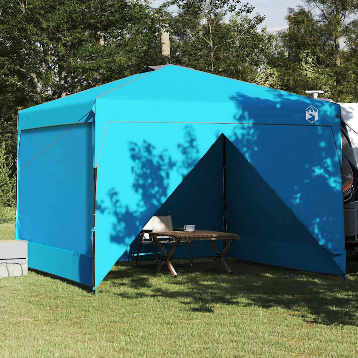 Una tenda pop-up blu è allestita su un campo erboso. All'interno, un tavolino e una sedia. Alberi e un veicolo sullo sfondo.
