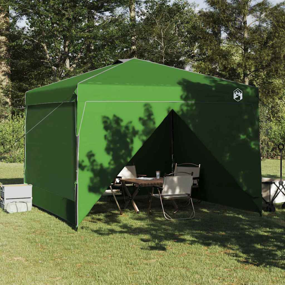 Tenda verde sull'erba. All'interno, un tavolo e sedie. Alberi sullo sfondo. Ombre sulla tenda. Frigorifero bianco a sinistra.