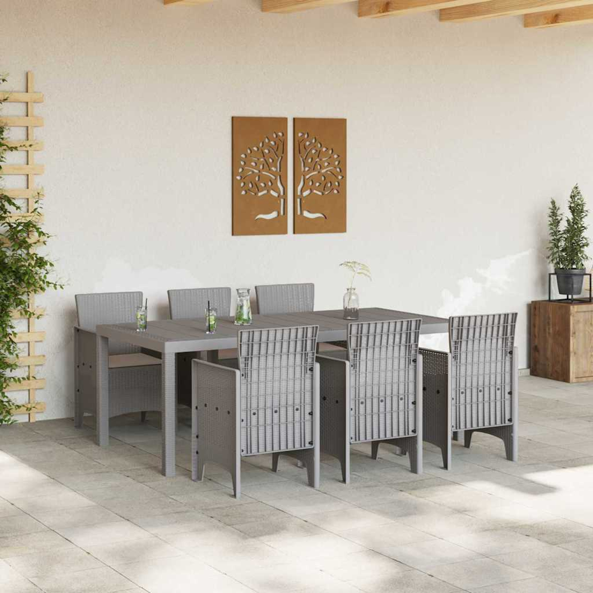 Juego de comedor al aire libre: mesa y sillas grises. Arte de árbol marrón en la pared. Plantas y bebidas en la mesa. Suelo de piedra.