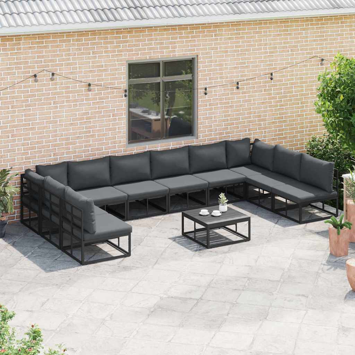 Un set da patio all'aperto con divano a U, cuscini e tavolino. Muro di mattoni e piante sullo sfondo.
