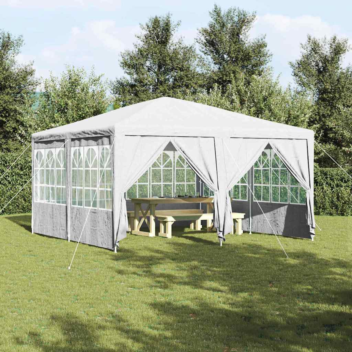 Un gazebo bianco con tende grigie e finestre si trova su erba verde. All'interno c'è un tavolo da picnic e panche in legno. Alberi sullo sfondo.
