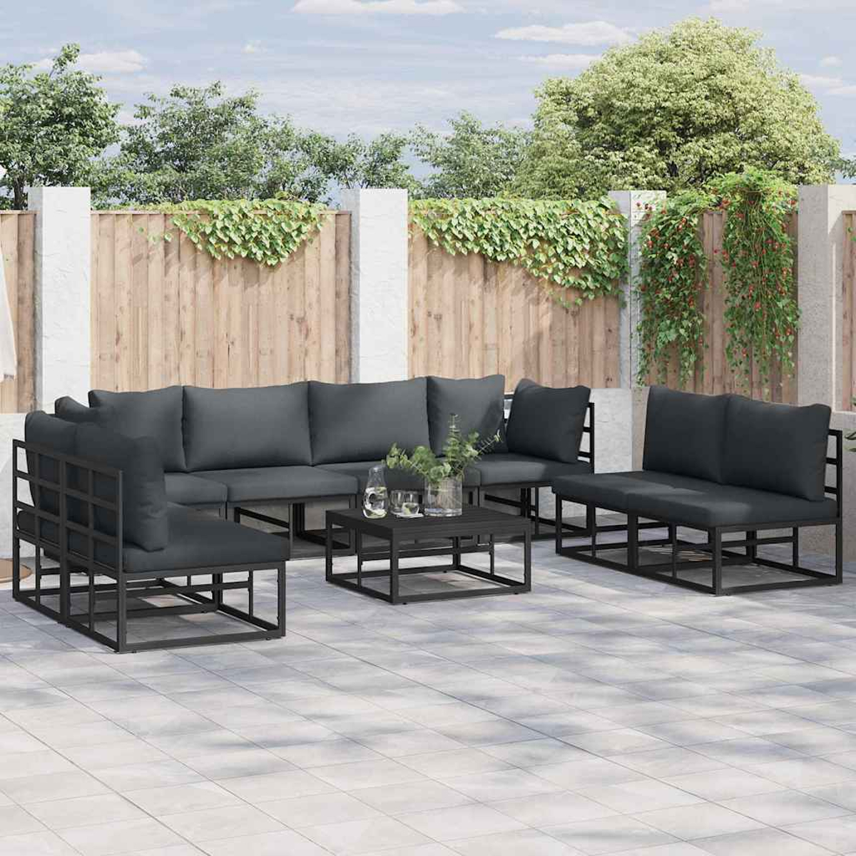 Gartenmöbel-Set. Graue Kissen auf schwarzen Metallrahmen. Enthält ein Ecksofa, Stühle und einen Couchtisch. Holzzaun im Hintergrund.