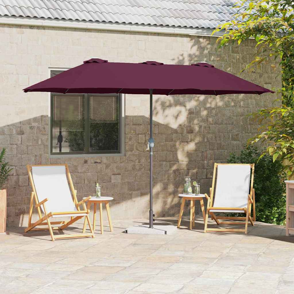 Una scena del patio con un ombrello bordeaux, due sedie a sdraio bianche, tavolini e un muro di pietra sullo sfondo.