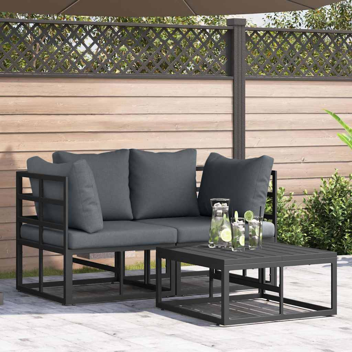 Szene im Freien mit grauem Sofa und Couchtisch. Getränke mit Limette stehen auf dem Tisch. Ein Zaun und Pflanzen sind im Hintergrund.