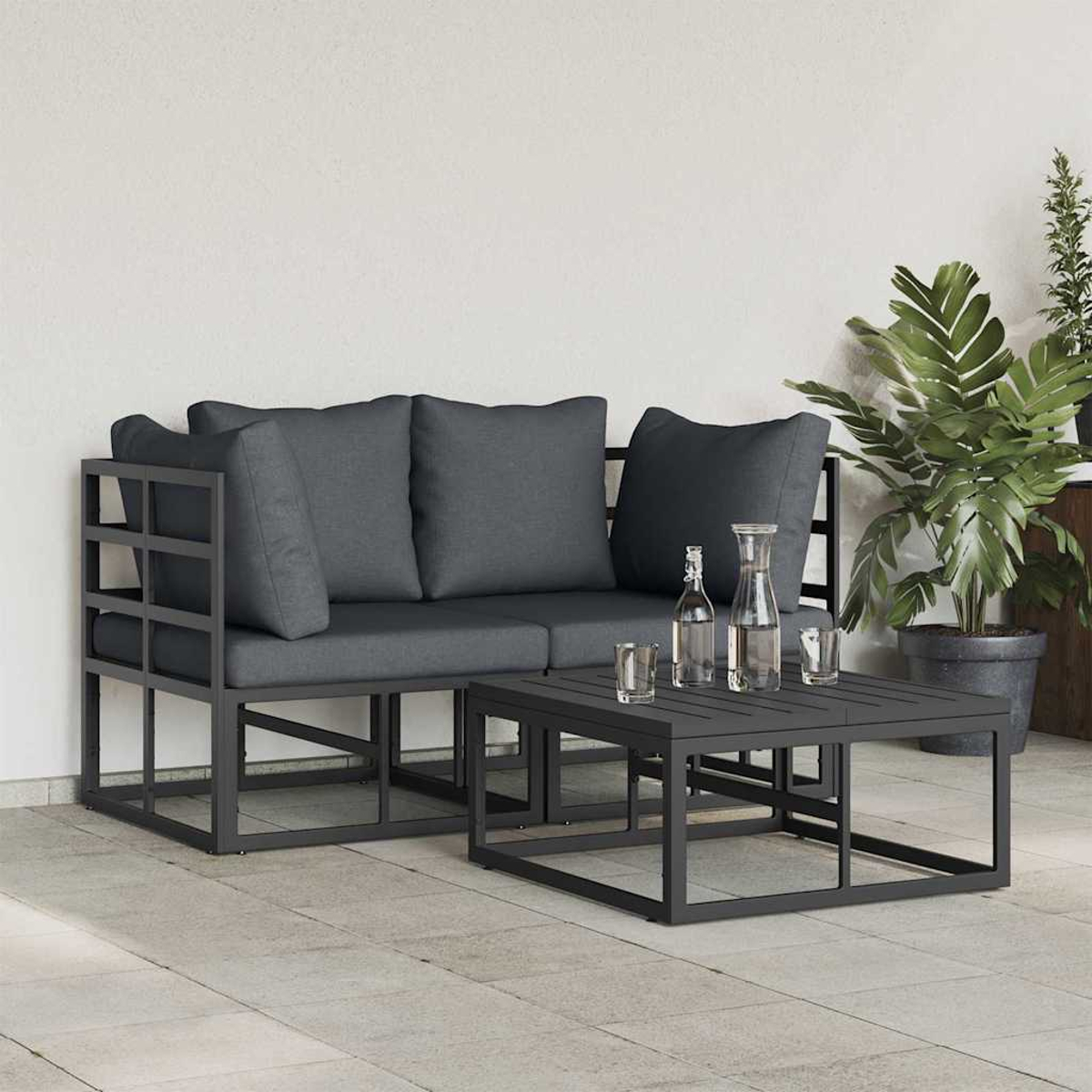 Graues Outdoor-Sofa und Tisch-Set mit Kissen, Gläsern und einer Pflanze. Die Szene spielt sich auf einer gefliesten Terrasse vor einer weißen Wand ab.