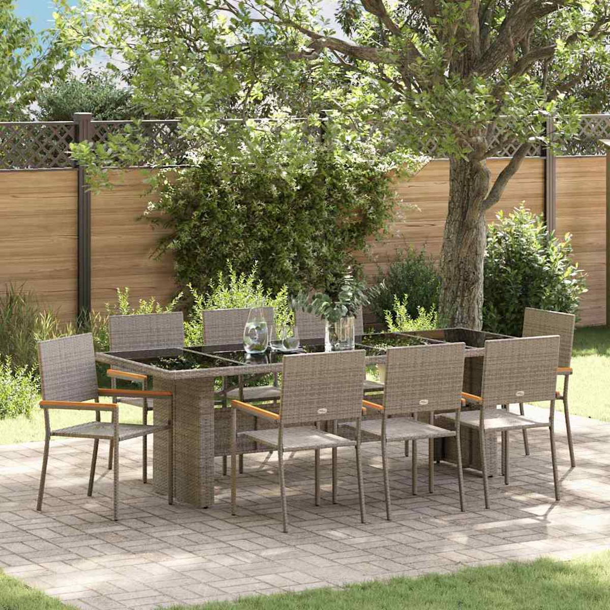 Juego de comedor al aire libre con mesa de cristal y sillas de mimbre. La escena incluye un árbol, una valla y un patio de ladrillos.