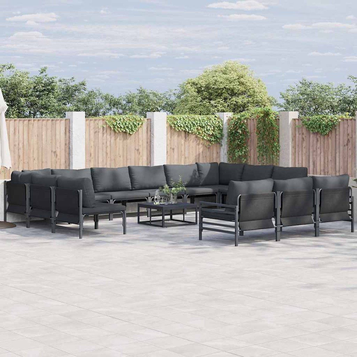 Outdoor-Sitzgruppe mit grauen Kissen und Metallrahmen. Inklusive Tisch. Im Hintergrund ein Holzzaun mit Grün.