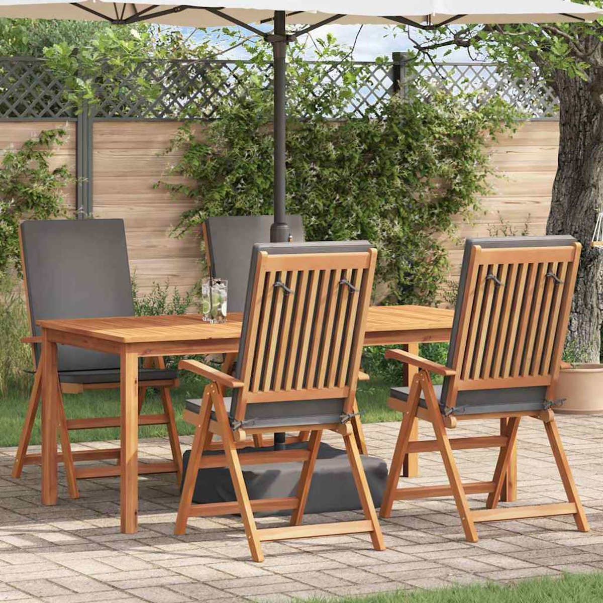 Juego de comedor al aire libre de madera con mesa, sillas y sombrilla en un patio. Cojines grises en las sillas. Follaje verde y valla de madera.