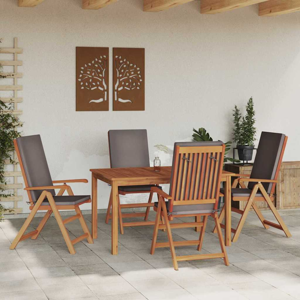 Juego de comedor al aire libre: mesa de madera, cuatro sillas con cojines grises. Arte mural con siluetas de árboles. Plantas en macetas.