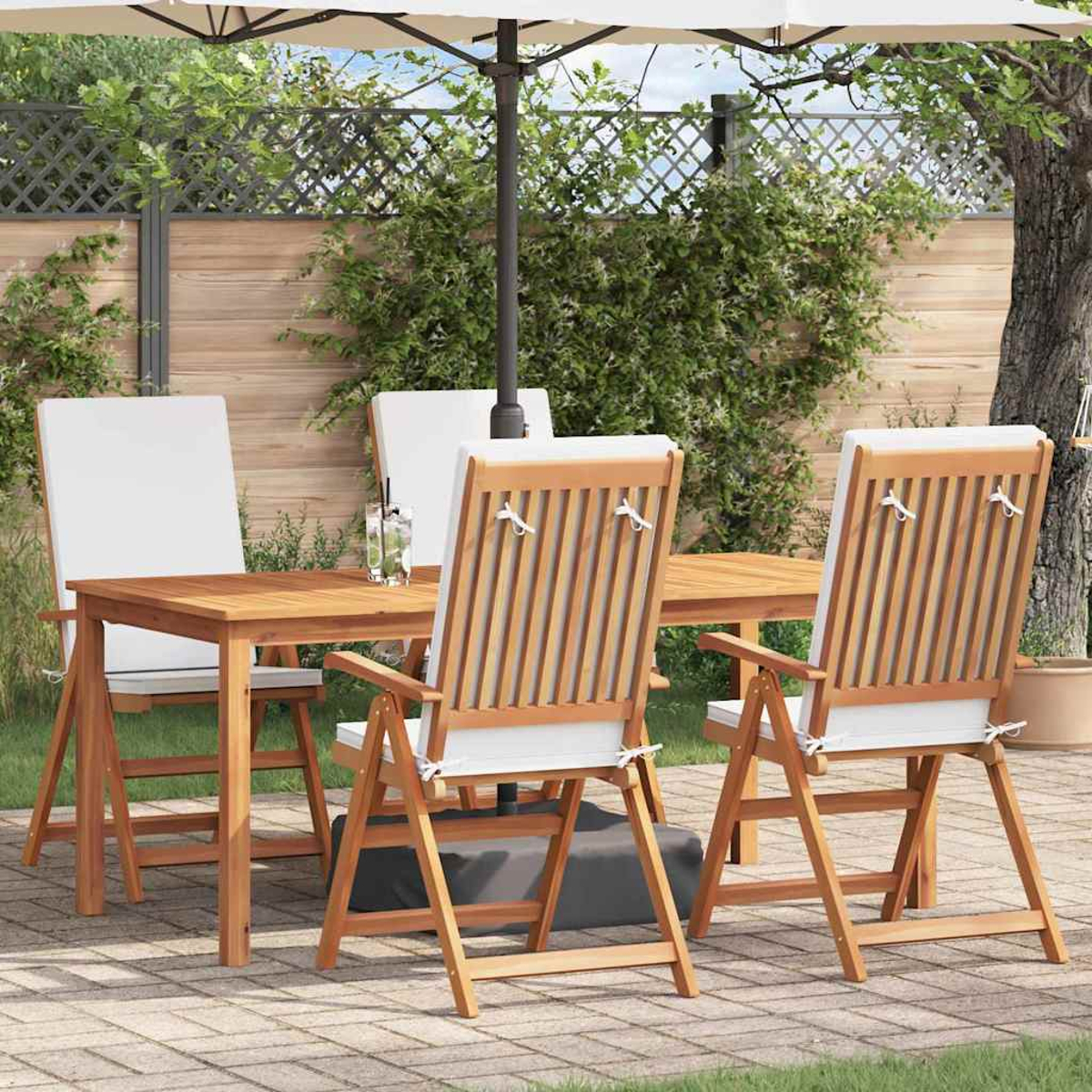 Szene im Freien mit Holztisch, Stühlen und Sonnenschirm. Weiße Kissen und Grün im Hintergrund auf einer Terrasse.