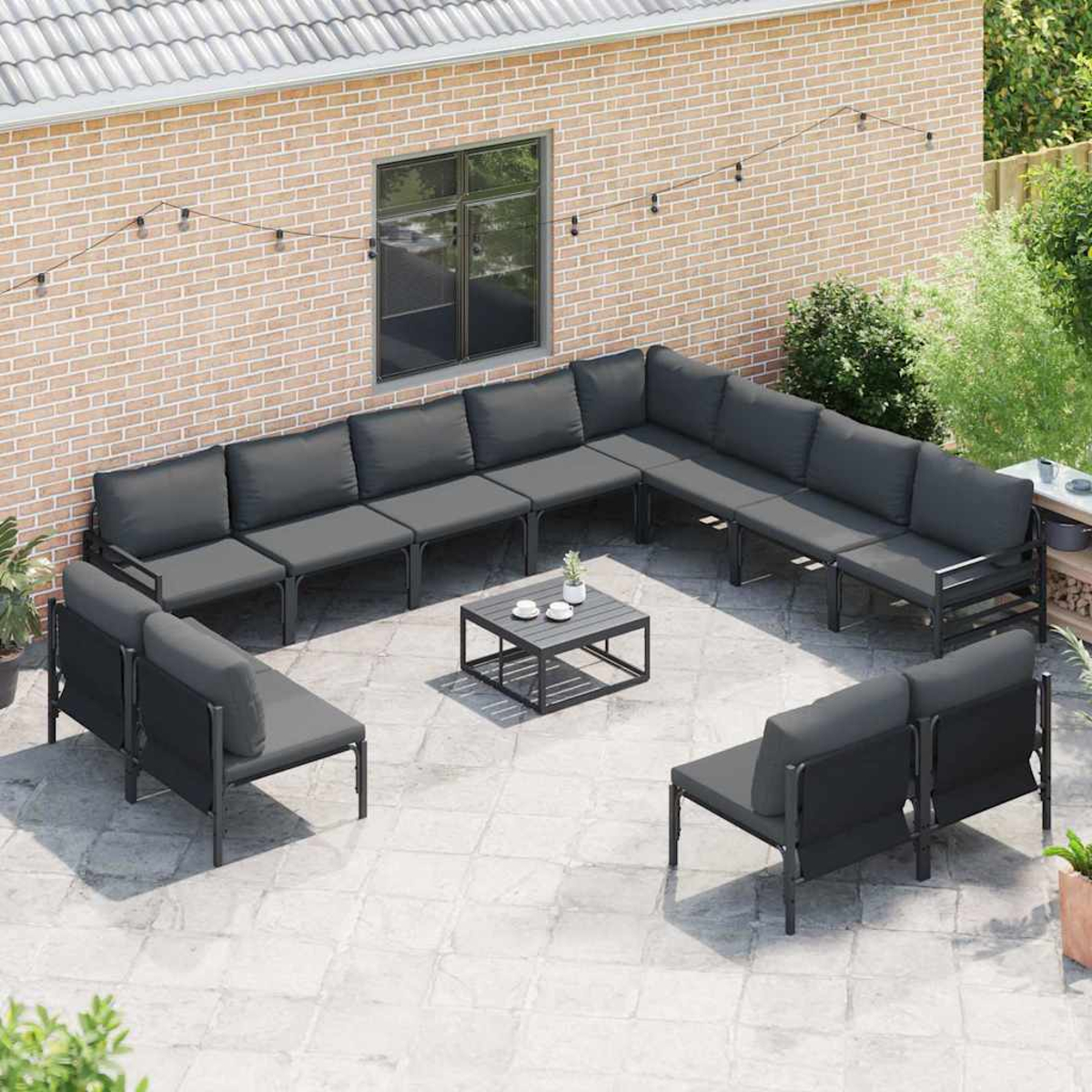 Garten-Sitzgruppe auf einer Terrasse. Enthält ein großes Ecksofa, zwei Loveseats und einen Couchtisch. Hintergrund Backsteinmauer.
