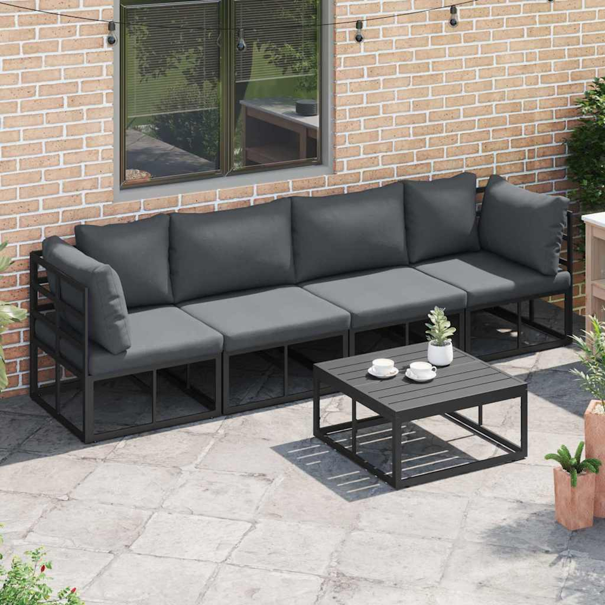 Terrasse mit dunkelgrauem Sofa, quadratischem Couchtisch und Backsteinmauer im Hintergrund.