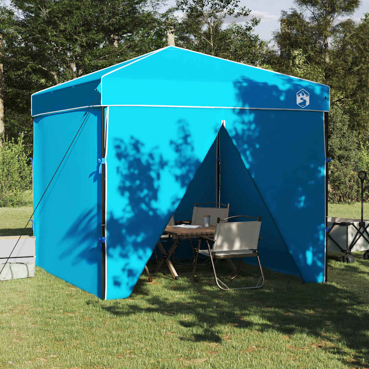 Tenda blu con davanti aperto, tavolo, sedie all'interno, sull'erba. Alberi sullo sfondo. Rifinitura bianca e un logo. Giorno soleggiato.