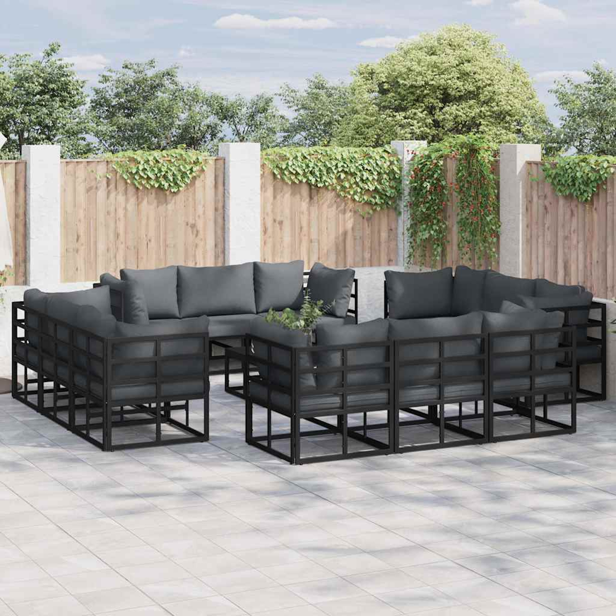 Set di sedute per esterni. Strutture in metallo nero con cuscini grigi. Su un patio piastrellato. Recinzione in legno e fogliame verde sullo sfondo.