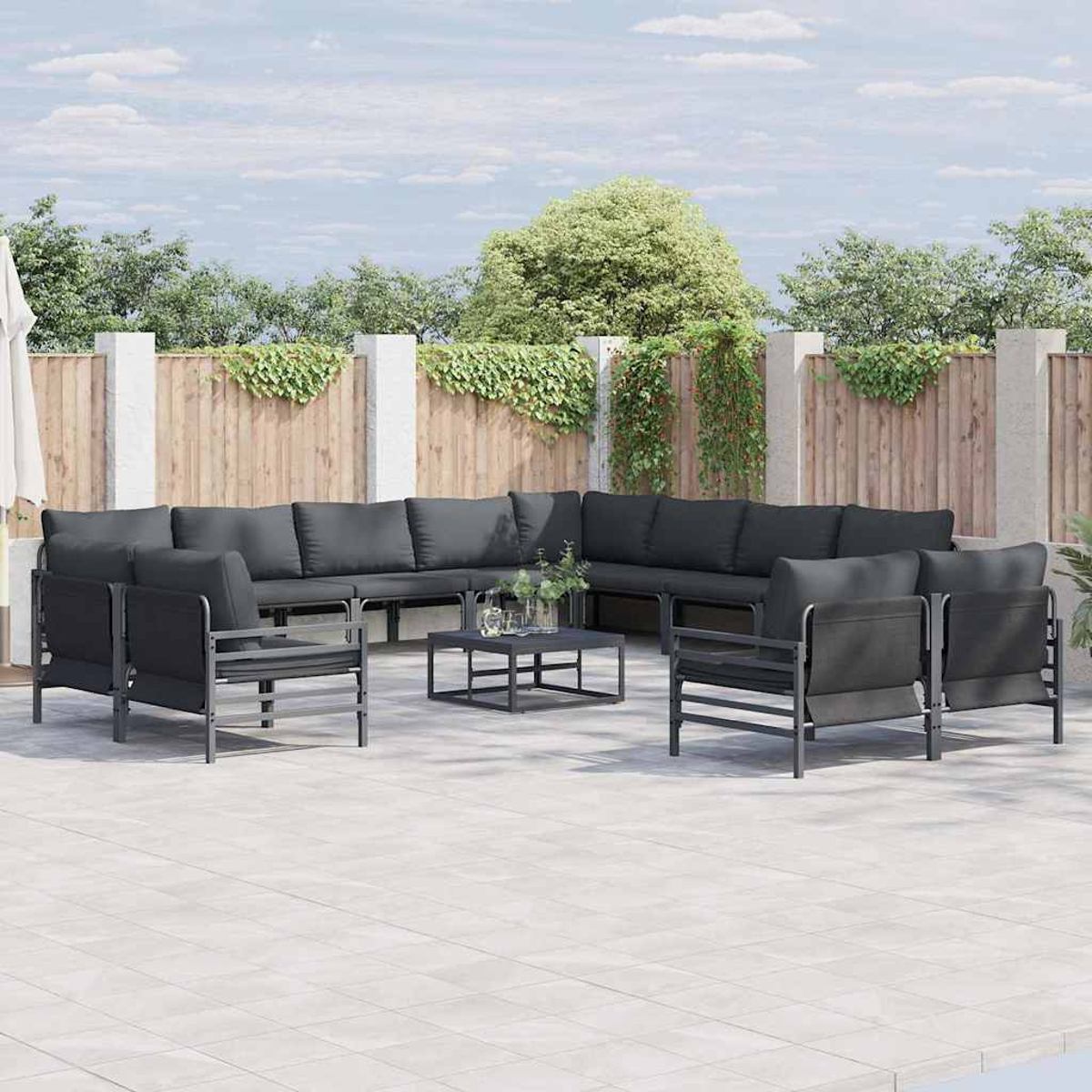 Garten-Sitzarrangement mit dunkelgrauen Kissen und Stühlen auf einer gefliesten Terrasse. Ein kleiner Tisch und ein Zaun sind im Hintergrund.