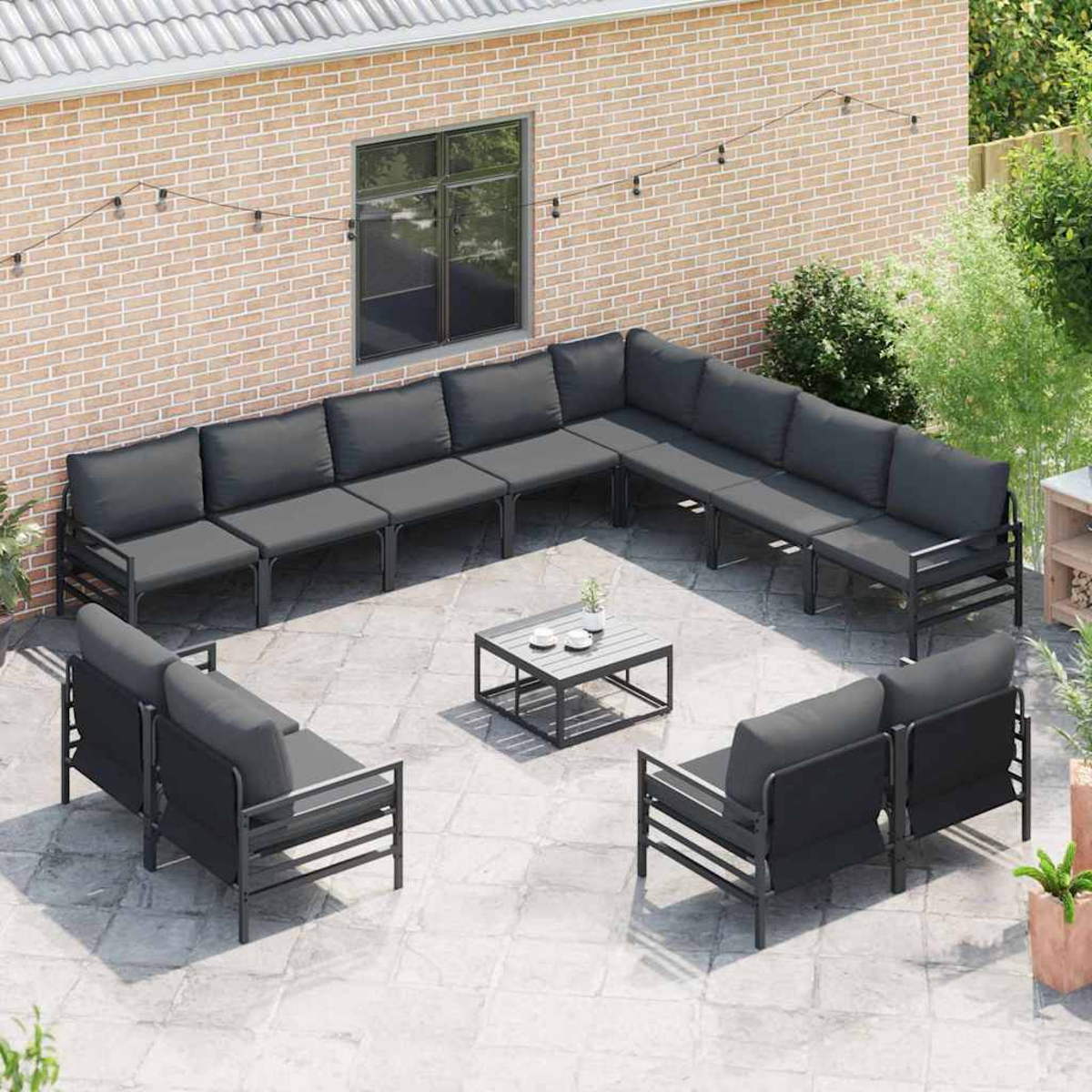 Terrassenset mit grauen Kissen und schwarzen Rahmen. Enthält ein Ecksofa, zwei Sessel und einen kleinen Tisch auf einer gefliesten Terrasse.